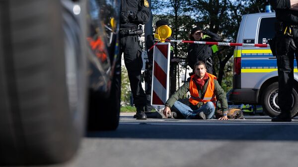 Polizeibeamte stehen neben einem Klimaaktivisten, der sich in der Münchner Innenstadt auf die Fahrbahn geklebt hat., © Sven Hoppe/dpa