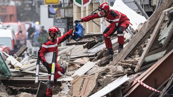 Zwei Rettungskräfte reichen sich Werkzeuge inmitten der Trümmer eines eingestürzten Gebäudes., © Sameer Al-Doumy/AFP/dpa