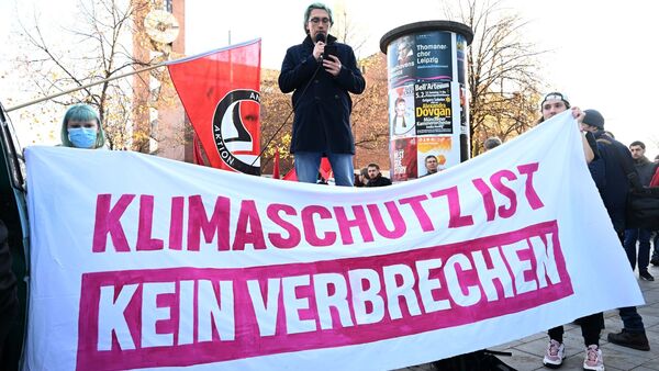 Ein Demonstrant spricht hinter einem Banner mit der Aufschrift «Klimaschutz ist kein Verbrechen»., © Felix Hörhager/dpa