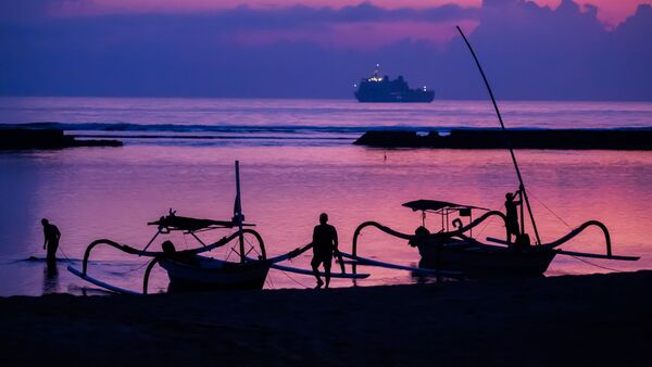 Männer befestigen vor Sonnenaufgang am Tag vor Beginn des G20-Gipfels am Strand von Nusa Dua Boote, wobei im Hintergrund ein Schiff der indonesischen Marine zu sehen ist., © Christoph Soeder/dpa