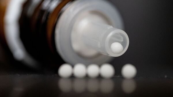 Homöopathische Kugeln liegen vor einer Spenderflasche auf einem Tisch., © Marijan Murat/dpa