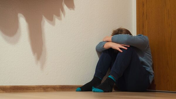 Ein Junge kauert sich in der Ecke seines Zimmers am Fußboden sitzend zusammen., © Nicolas Armer/dpa/Symbolbild